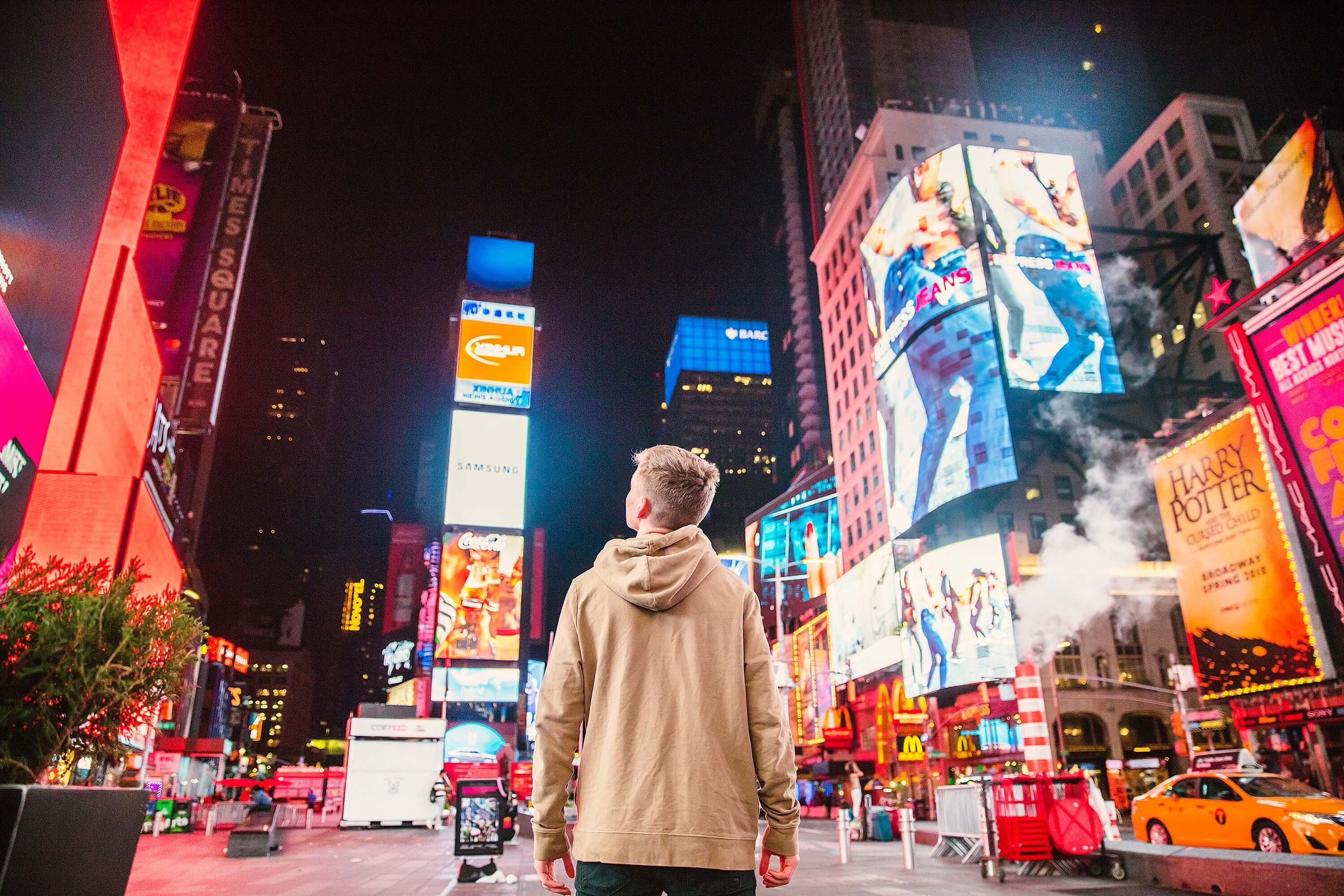 man standing on road in front of high-rise building surrounded by digital billboard ads